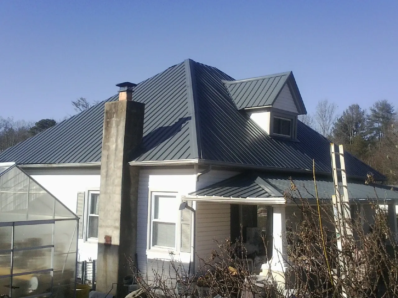 Dark blue standing seam metal roof on a white farmhouse with dormer — Slate & Tile Roof Repair by Roofing Brothers in Juneau