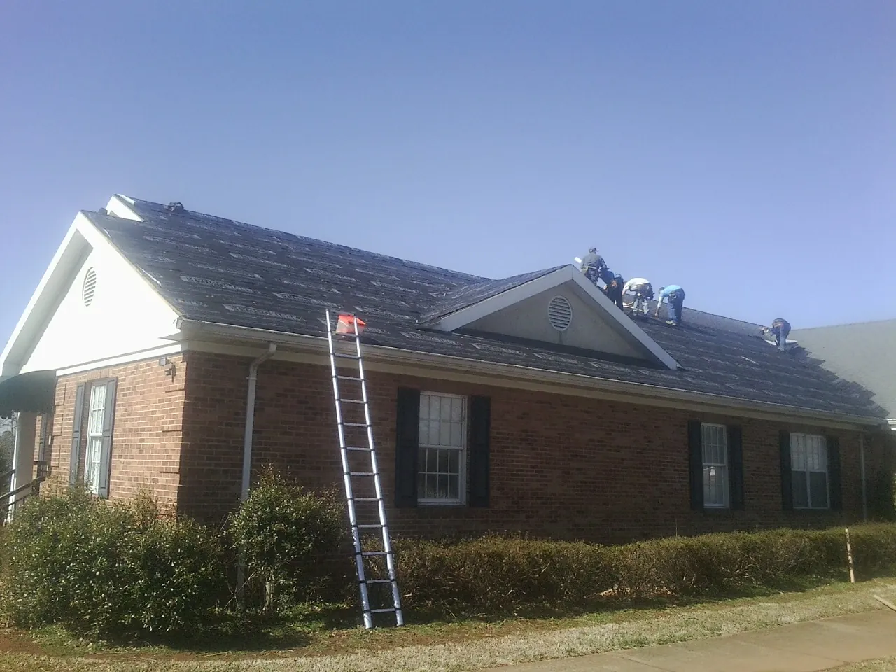 Crew tearing shingles off a brick ranch roof with a ladder set — Metal Roof Repair work by our crew in Juneau