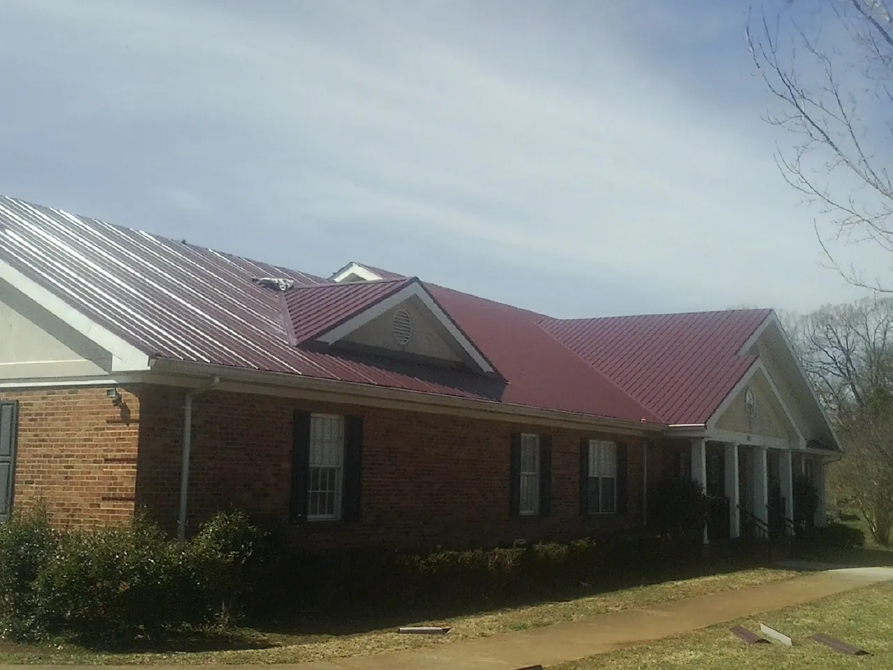 Red metal roof with gabled entries on a long brick building, from a Hail Damage Roof Repair job in Juneau