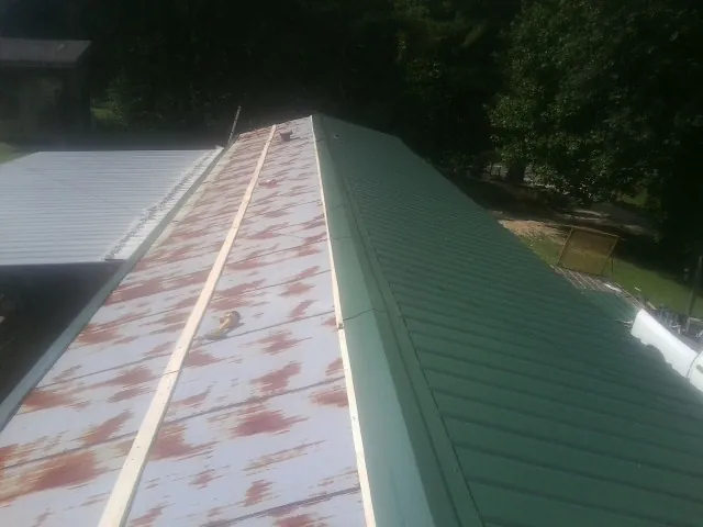 Old rusted panels beside newly installed green metal roofing — Wind Damage Roof Repair by Roofing Brothers in Juneau