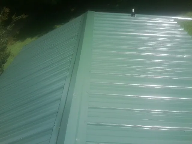New green metal panels meeting at the ridge of a roof — Flat Roof Repair work by our crew in Juneau