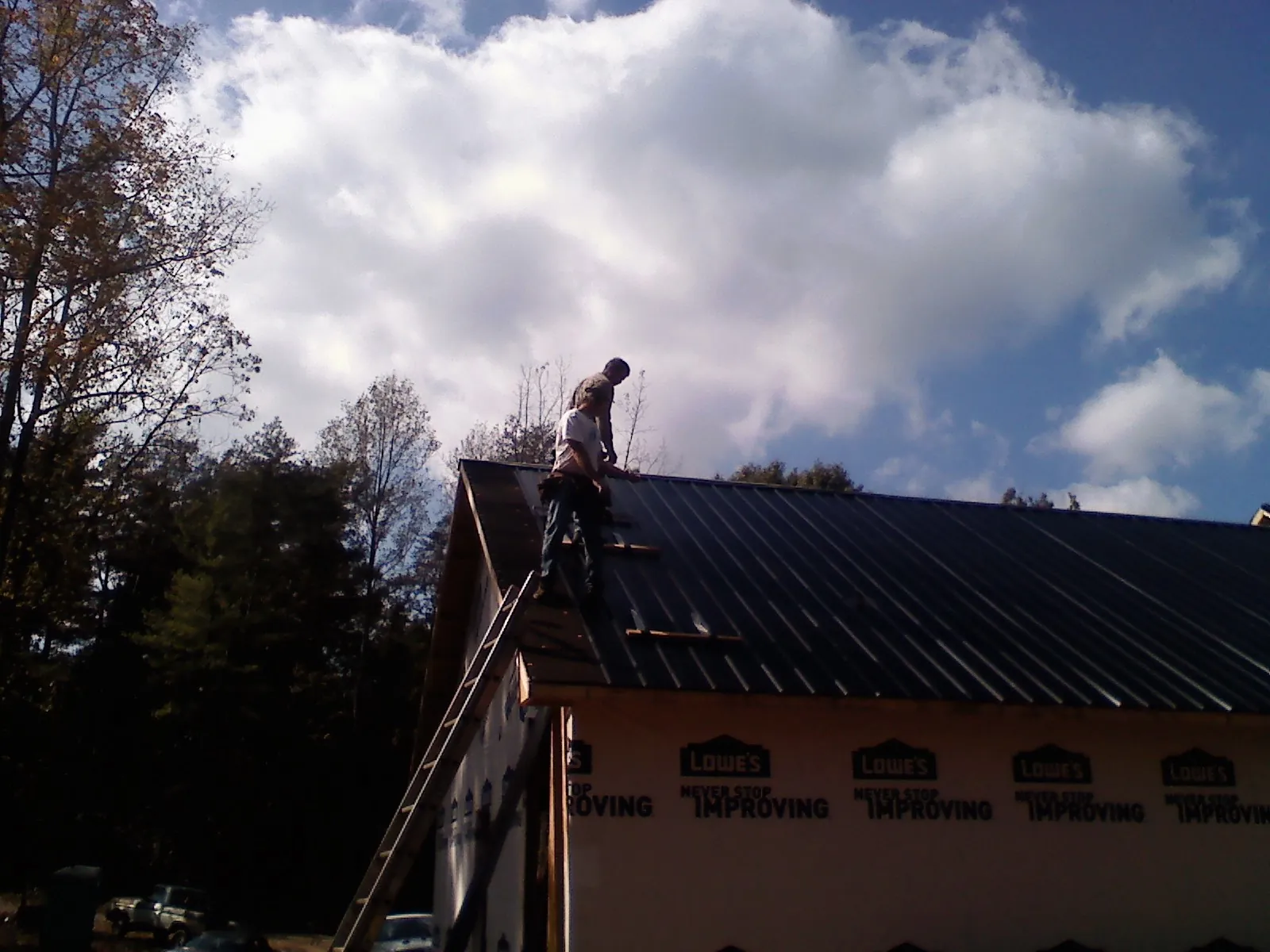 Roofer fastening dark metal panels high against a cloudy sky, from a Roof Inspection job in Juneau