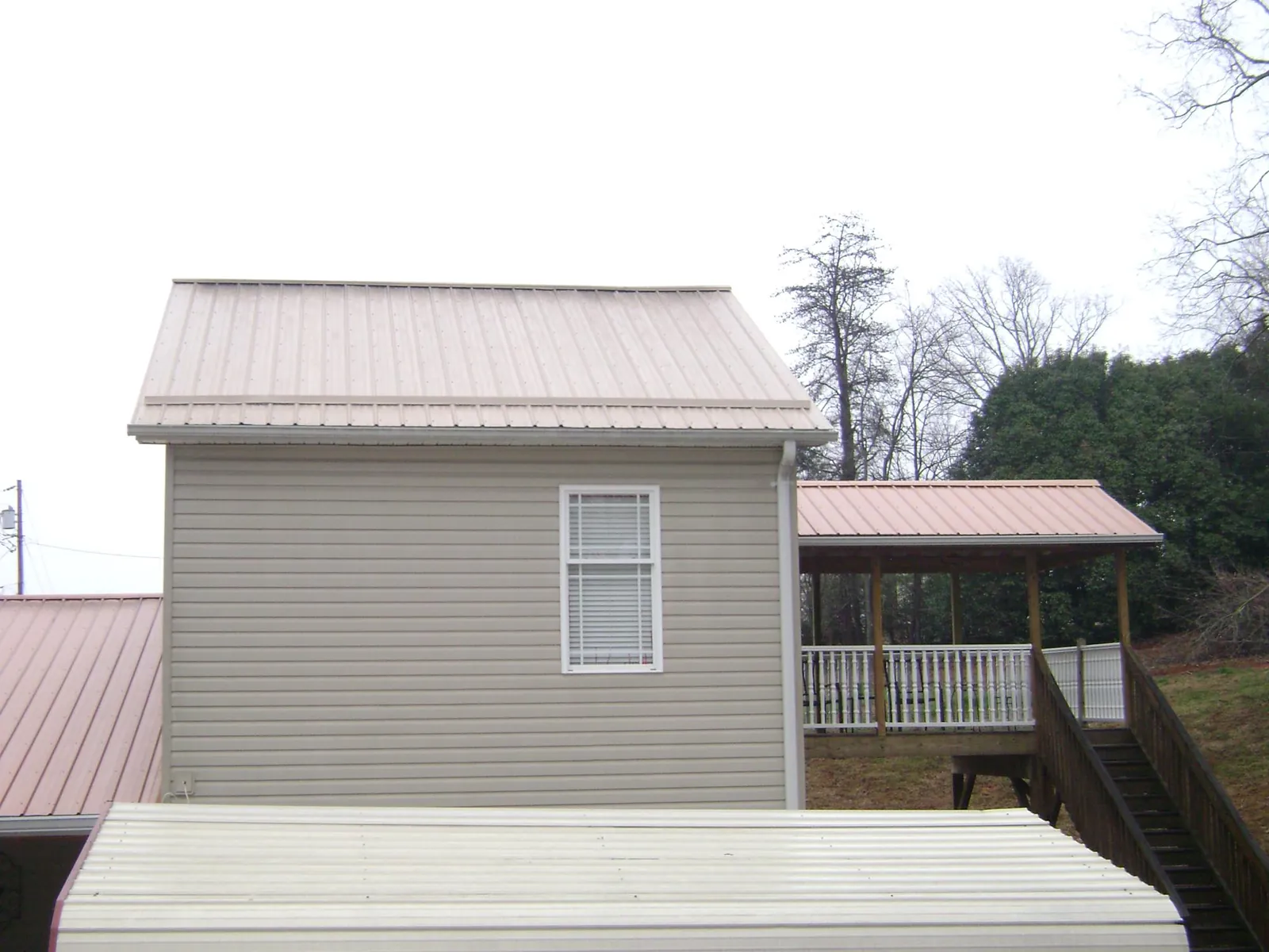 Tan metal roofs on a two story addition and attached porch, from a Roof Replacement job in Juneau